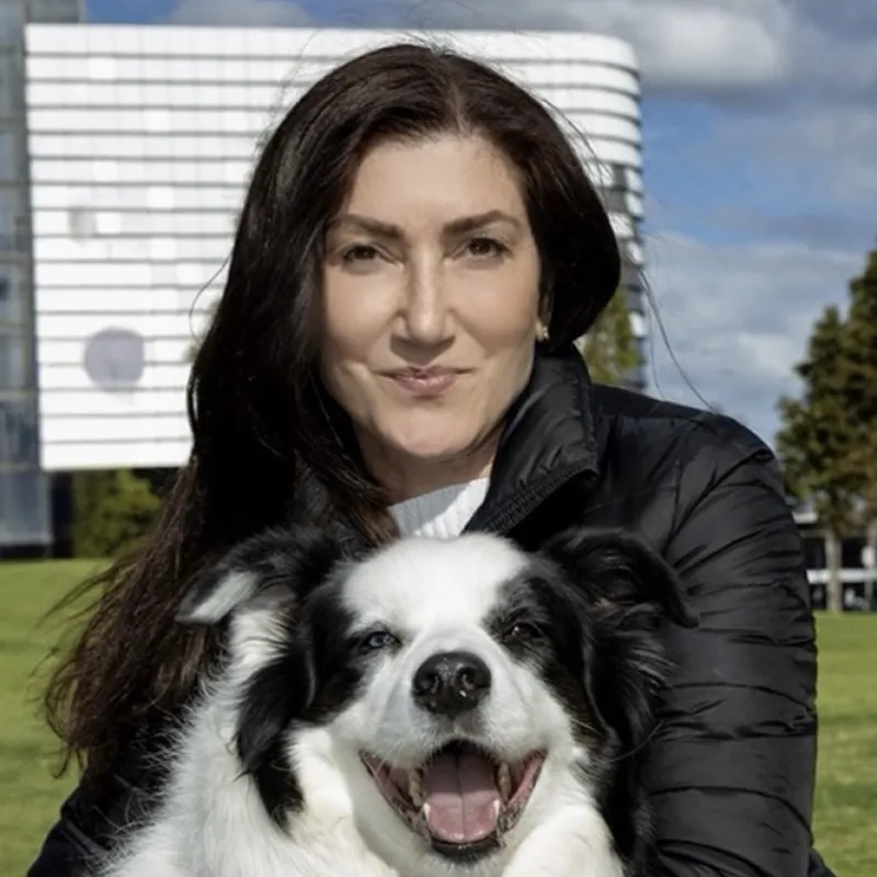 Ayda holding her black and white border collie Archie outdoors in a park, both looking at the camera